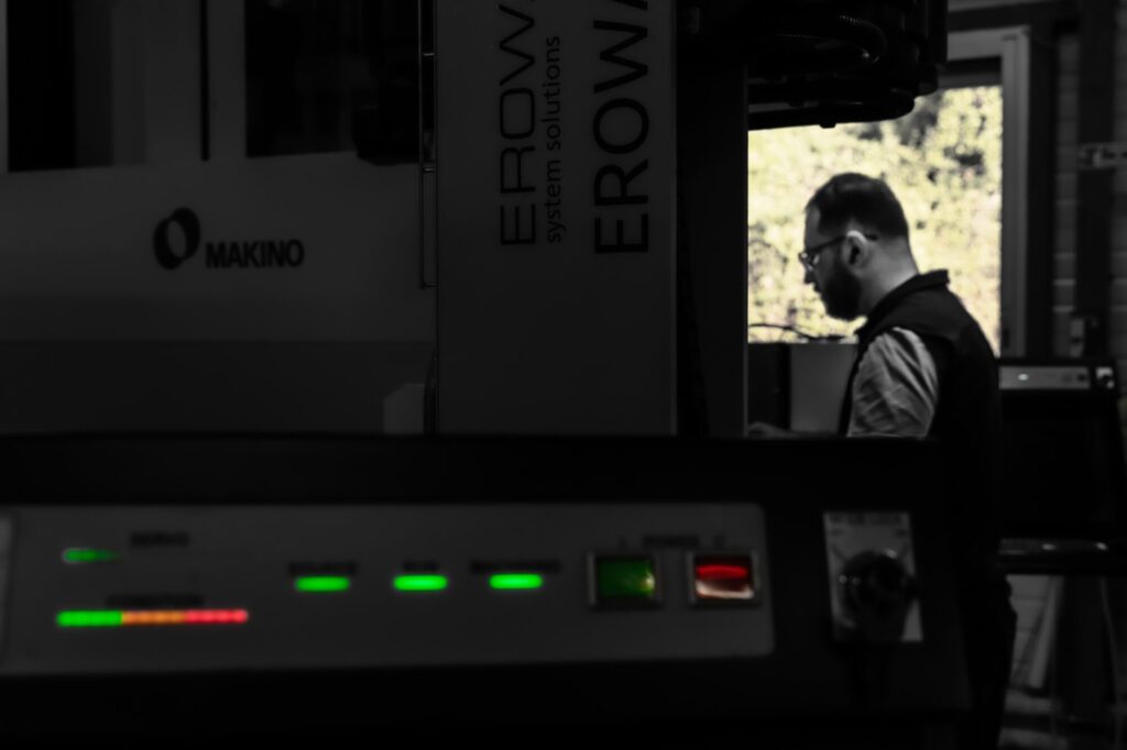 Mr ben - Entre ombre et clarté, la silhouette de l’opérateur apparaît au milieu des machines. Les voyants lumineux ponctuent l’image comme les battements silencieux d’un atelier en activité. Cette photographie met en lumière ce qui reste souvent invisible : la vigilance, l’expertise et la présence humaine qui donnent du sens à la technologie, (35mm,f5.6,ISO250,1/125sec
