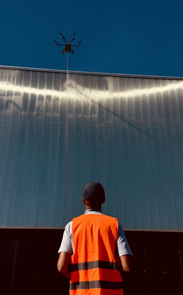 Yassine - L'opérateur L'opérateur guide son drone avec précision face à la façade. La technologie permet d'accéder à des endroits difficiles, dessinant une silhouette futuriste et efficace sous un ciel bleu parfait.