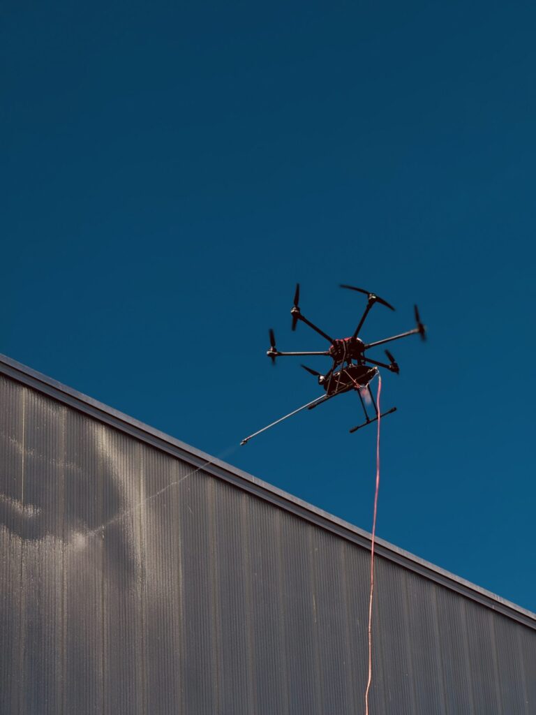 Yassine - Le Face à face L'innovation technologique rencontre l'immensité d'une façade industrielle sous un ciel d'un bleu parfait. Une image épurée qui capture toute la légèreté et la précision du drone face à la grandeur de l'infrastructure.