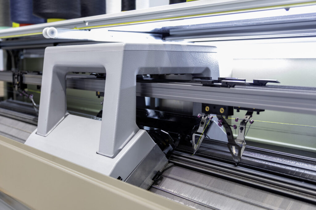 Lucillle - Le tricotage en forme Alignées au cœur de l’atelier, ces machines innovantes tricotent en toute autonomie des pièces de maille tridimensionnelles et sans coutures.  En concevant chaque pièce directement aux dimensions exactes, cette technologie novatrice élimine toute chute de matière, conjuguant performance technique et sobriété industrielle.