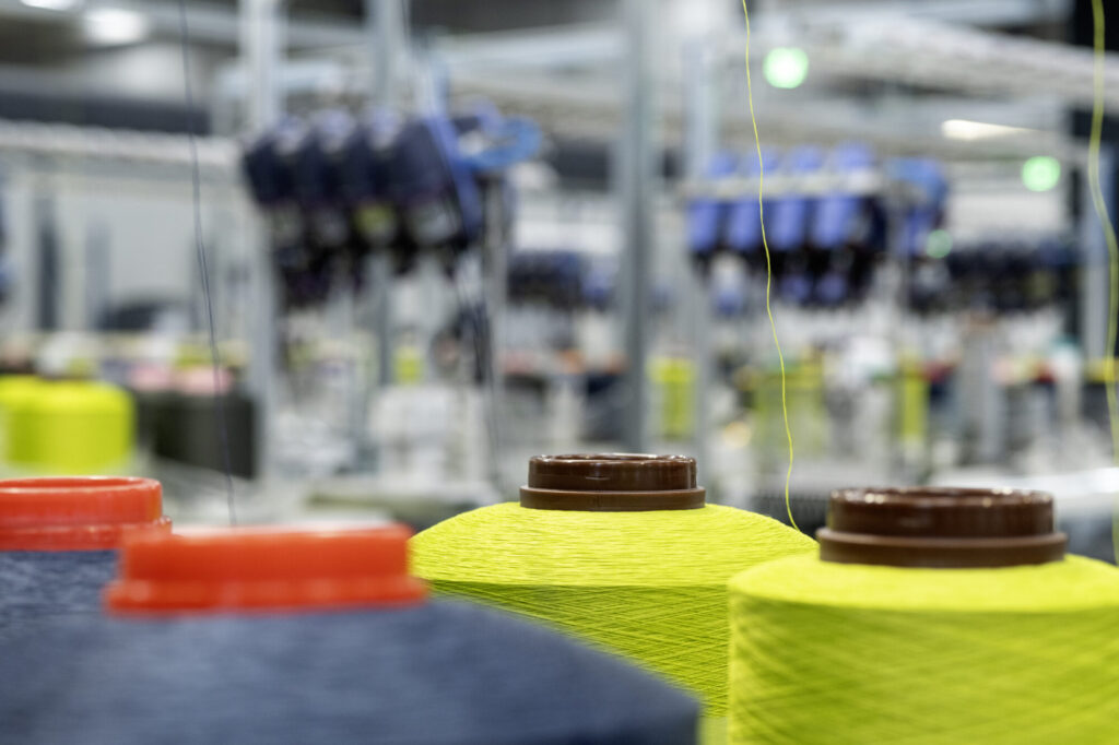 Lucillle - De la bobine à l'aiguille : Les bobines sont installées sur la machine avant que les fils ne soient acheminés avec précision vers l'entrée de la tricoteuse. Cette étape d'enfilage s'avère déterminante : un approvisionnement en fil imparfait entraîne l'arrêt immédiat de l'équipement et déclenche une alerte, nécessitant l'intervention rapide d'un opérateur pour résoudre le dysfonctionnement.